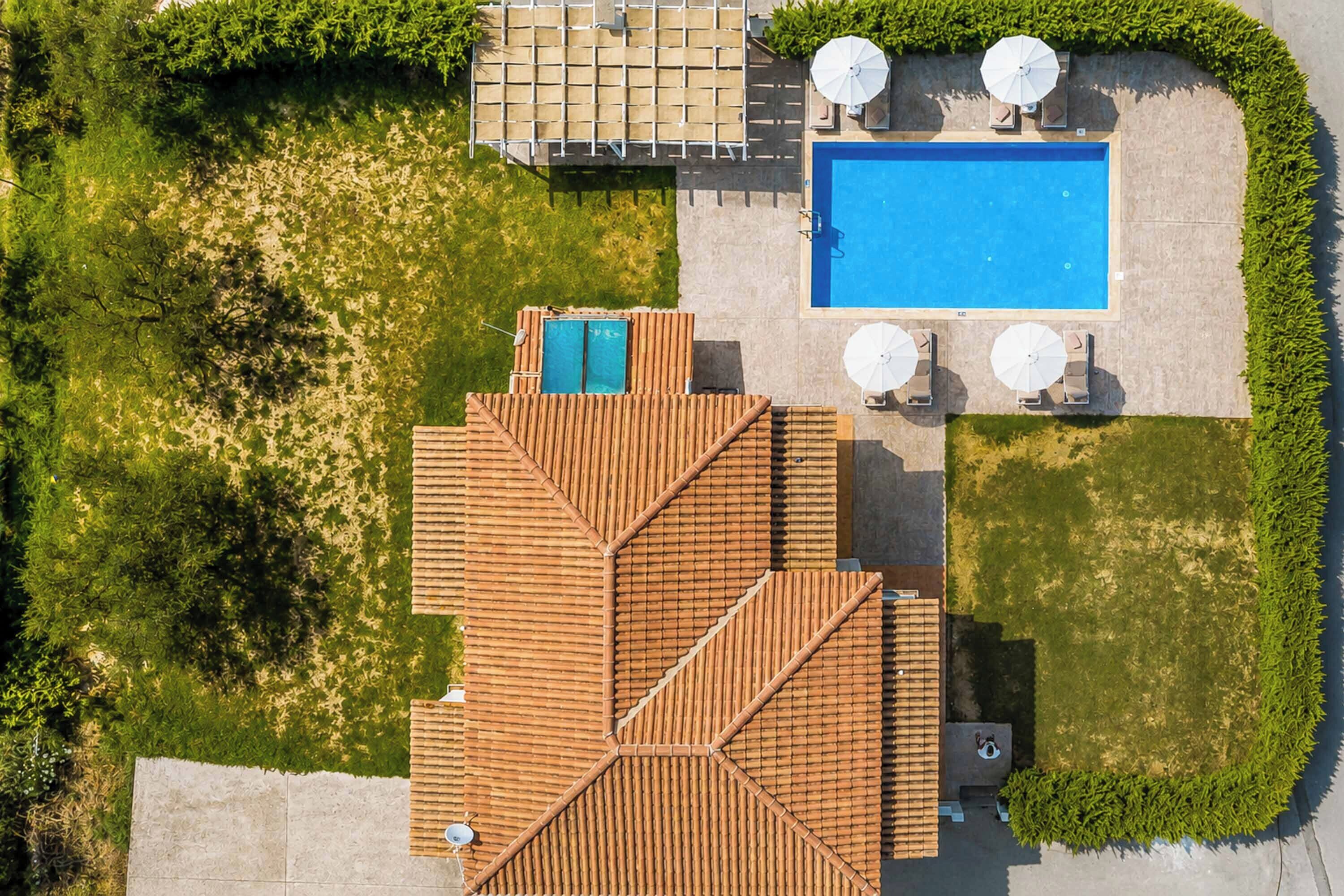 An aerial view of a property with a swimming pool, outdoor seating, and a wooden deck.