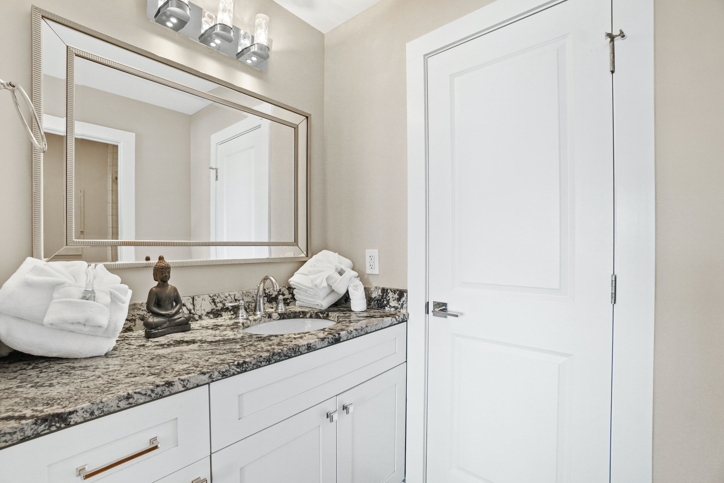A bathroom with a marble sink, a large mirror, a Buddha statue, and a white door.