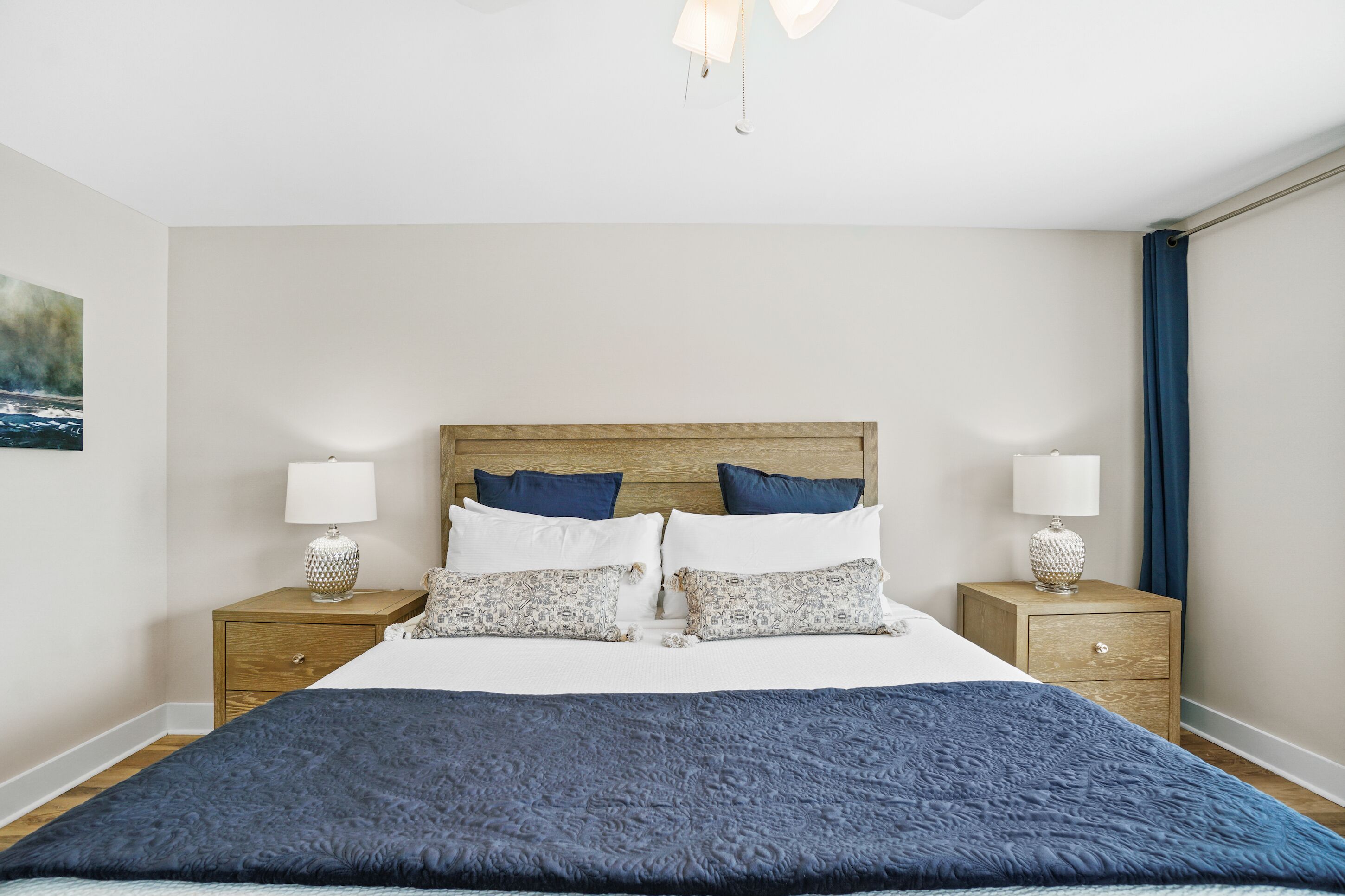 Un dormitorio ordenado con una cama grande, dos mesitas de noche con lámparas y un cuadro en la pared.