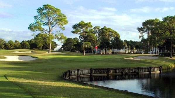 A golf course with sand bunkers, a water hazard, and a wooden bridge.