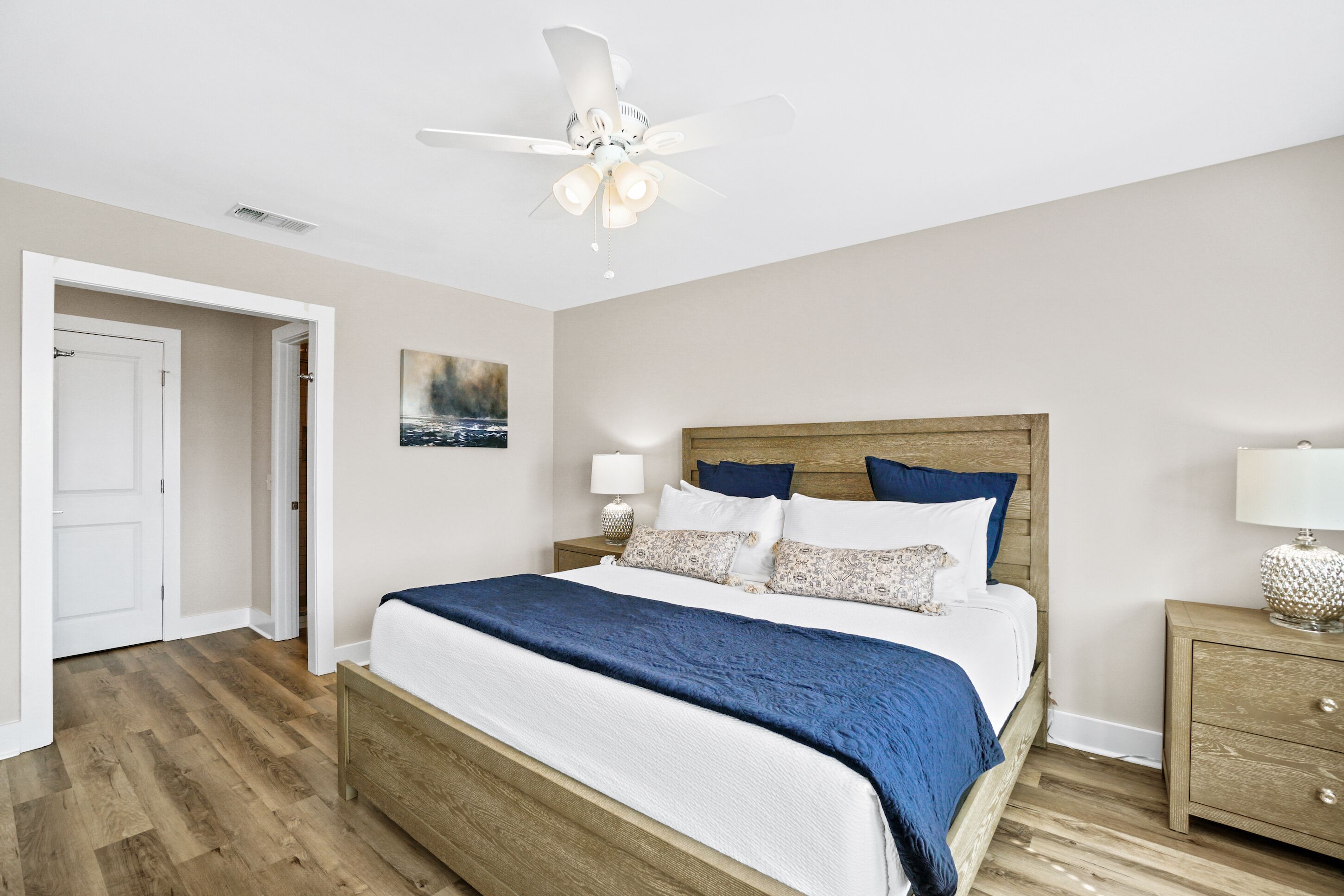 A bedroom with a bed, a ceiling fan, a nightstand, and a door.