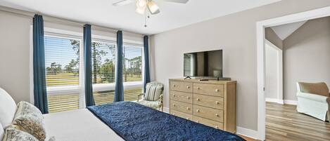 Camera da letto con un letto grande, una ventola a soffitto, un comò, una TV e vista sull'esterno.