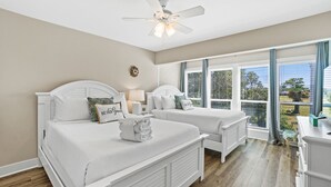 Ein Schlafzimmer mit zwei Betten, einem Deckenventilator und großen Fenstern mit Jalousien.