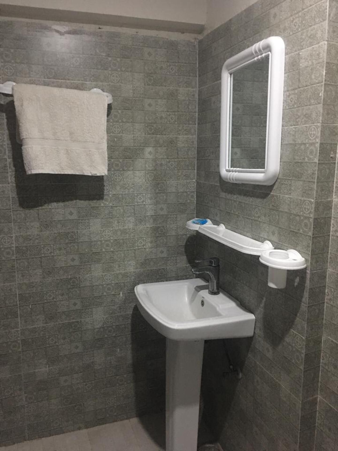 Une salle de bain avec un lavabo blanc, une serviette accrochée au mur et un miroir au-dessus du lavabo.