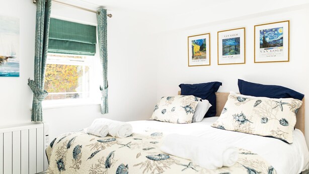 Una cama bien hecha con ropa de cama floral, una ventana con cortinas y tres cuadros en la pared.