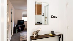 Un pasillo con un espejo, una pequeña mesa con un objeto decorativo y un televisor al fondo.