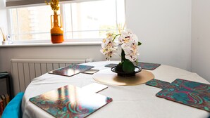 Una mesa redonda para comer con mantel blanco, un jarrón con orquídeas blancas y platos decorativos con estampado de paisley.