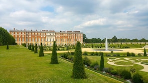 A large, historic building with a symmetrical facade, a central fountain, and a well-manicured garden with geometric landscaping.