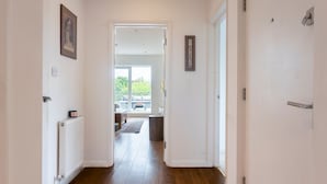 Un pasillo con piso de madera, paredes blancas y vista a una sala de estar con un sofá y una mesa de centro.