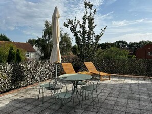 An outdoor patio with a round table and four chairs, a covered umbrella, and two wooden lounge chairs.