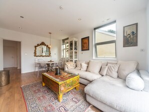 A spacious living room with a large sofa, a coffee table, and a dining area with chairs and a table. - Luxurious Flat with Large Private Terrace - Pass the Keys (Hampton Court)