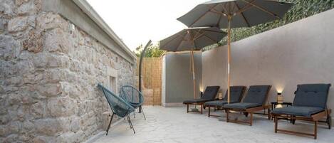 Zona de piscina con sillones de descanso y sombrillas, muros de piedra y una vista despejada a la piscina.