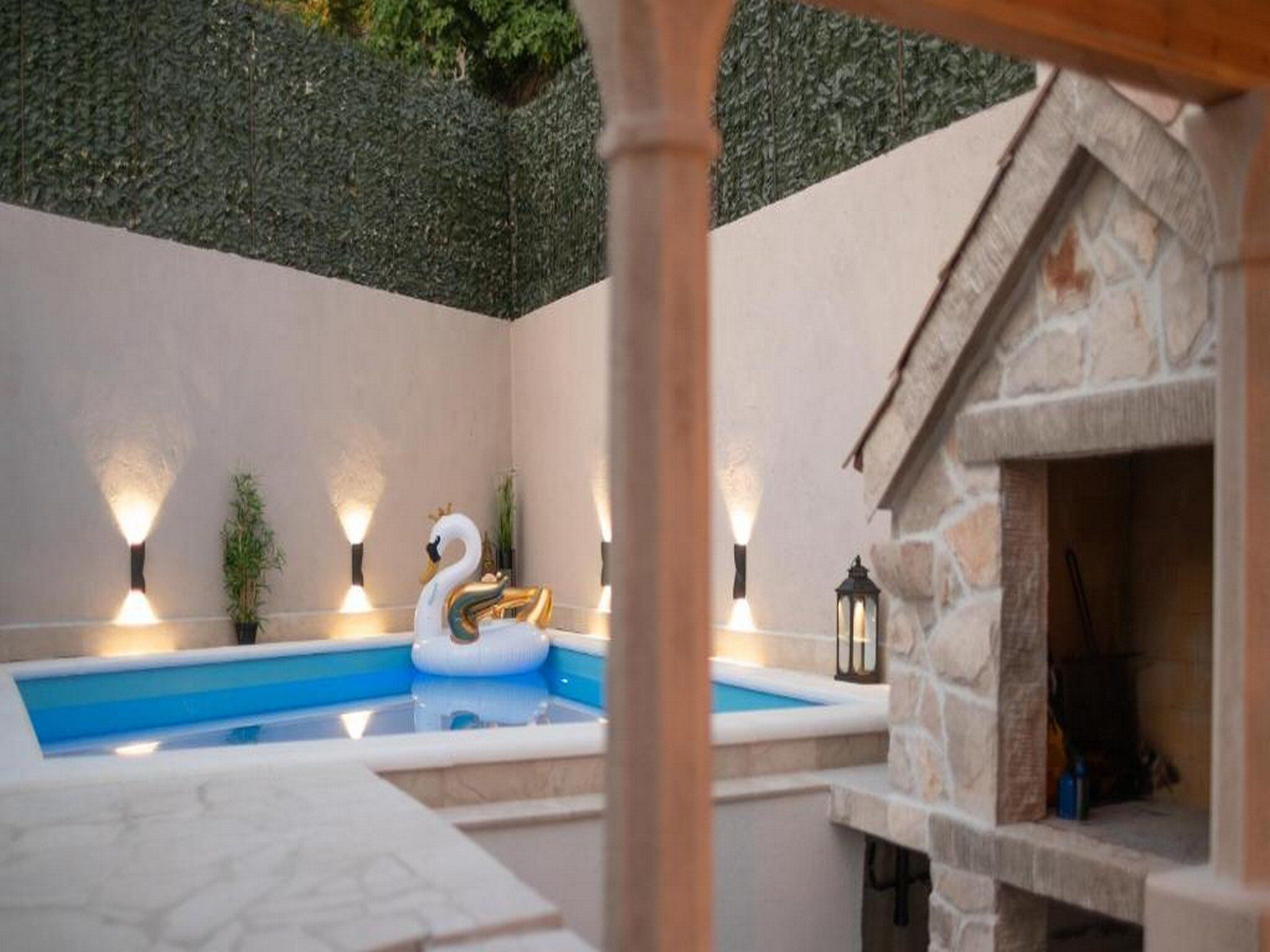 A swimming pool with a swan float, surrounded by stone walls and decorative lighting.
