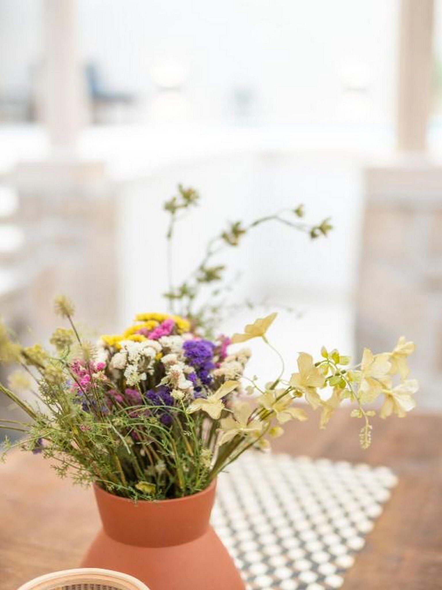 Un jarrón de terracota con un ramo de flores variadas sobre una mesa de madera.