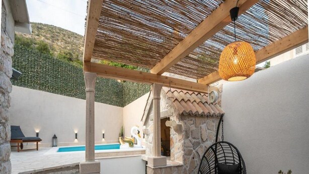 A covered outdoor area with a pool, stone walls, and a hanging chair. - House of Nice Memories (Orebic)