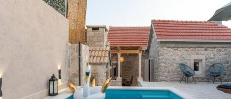 A swimming pool with a swan float, stone walls, and a red-tiled roof.