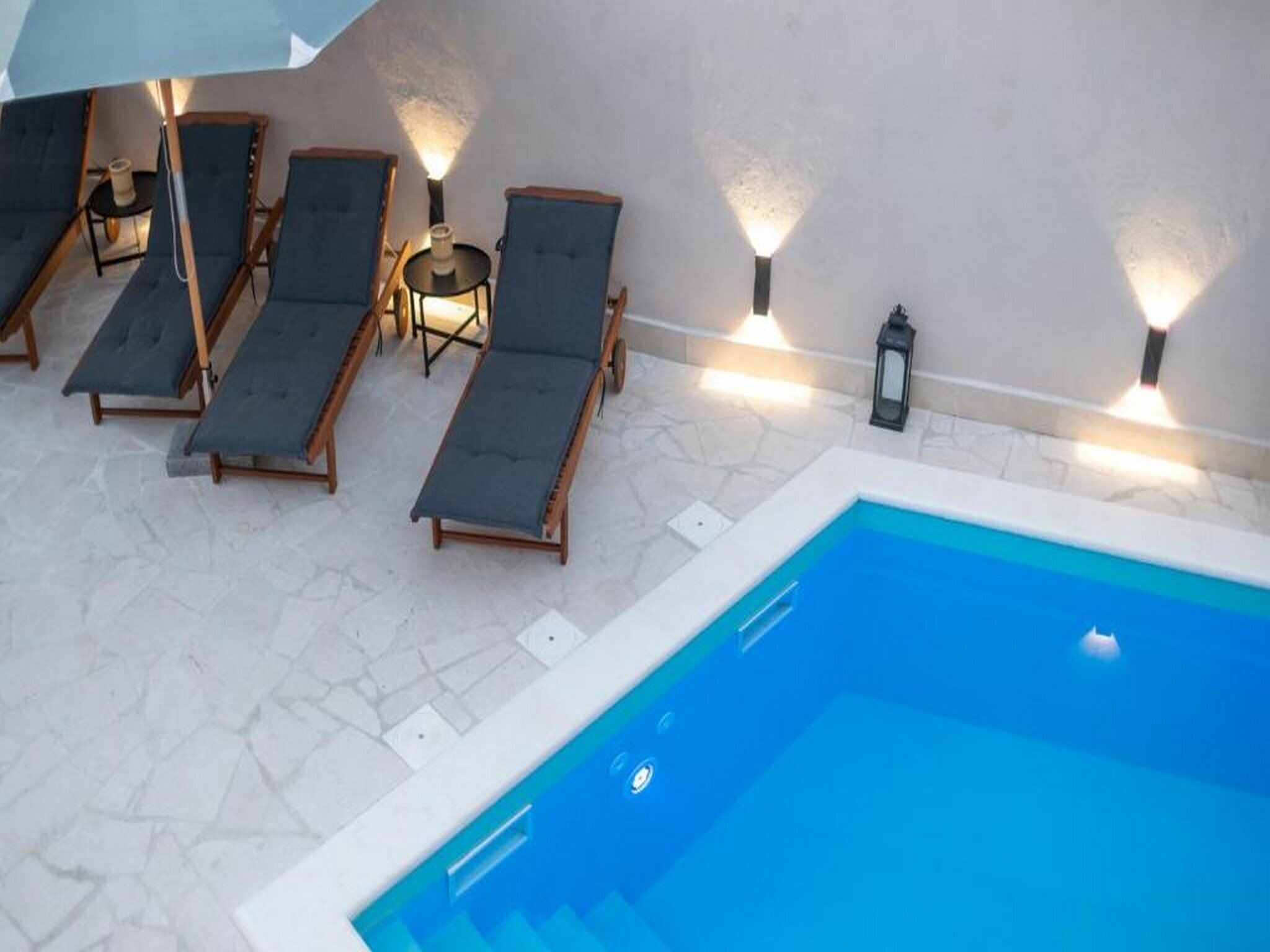 A poolside area with lounge chairs and wall-mounted lights.