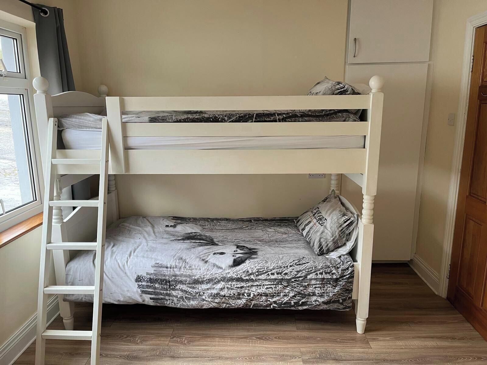 A bunk bed with a ladder, a window with curtains, and a wooden door.