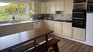 A modern kitchen with white cabinets, a built-in oven, and a dining area with a wooden table and bench. - 6 Ensuite Bedrooms-sleeps 12-garden-sea & Mtn View (Blackwater Bridge)