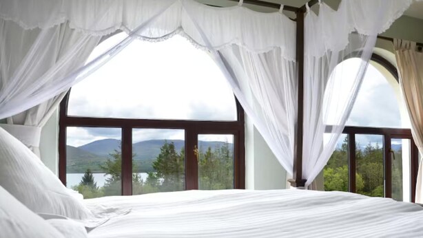 A bed with white linens, a canopy, and a view of mountains and trees through large windows. - 6 Ensuite Bedrooms-sleeps 12-garden-sea & Mtn View (Blackwater Bridge)