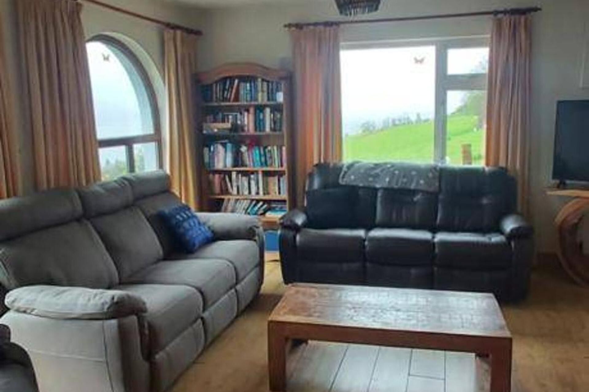 A living room with a grey sofa, a black sofa, a wooden coffee table, and a bookshelf.