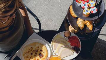 Une table dressée pour le petit-déjeuner, avec divers aliments, notamment une assiette contenant des œufs, des toasts et un verre de jus d’orange.