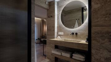 A modern bathroom with a marble vanity, a round mirror, and a built-in shelf with towels.