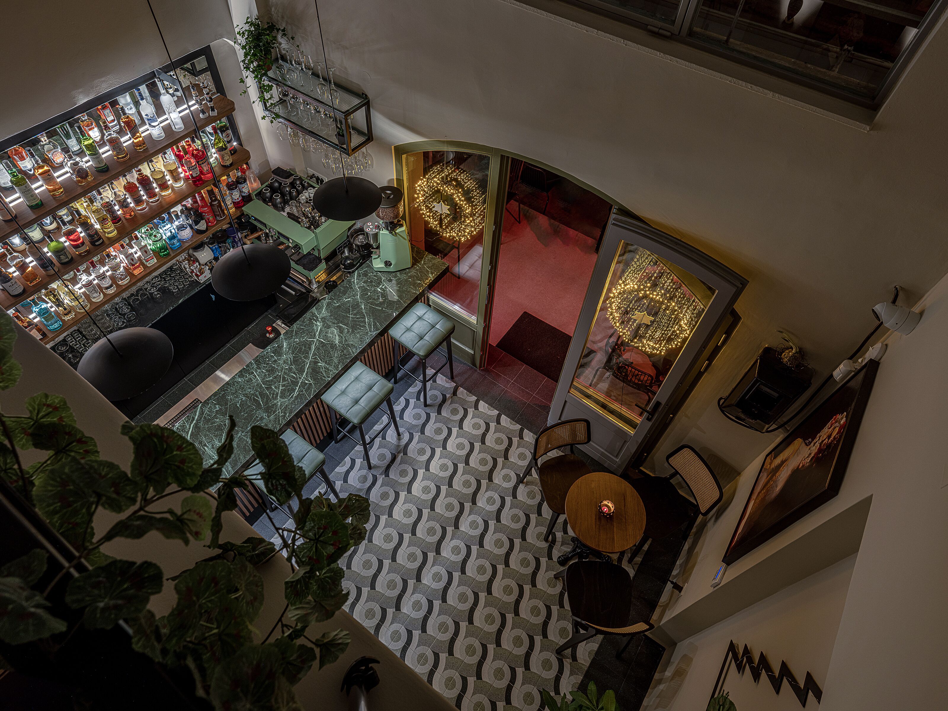 Un espace bar avec des étagères remplies de bouteilles et de verres, un coin salon avec des tables et des chaises, et un sol à motifs.