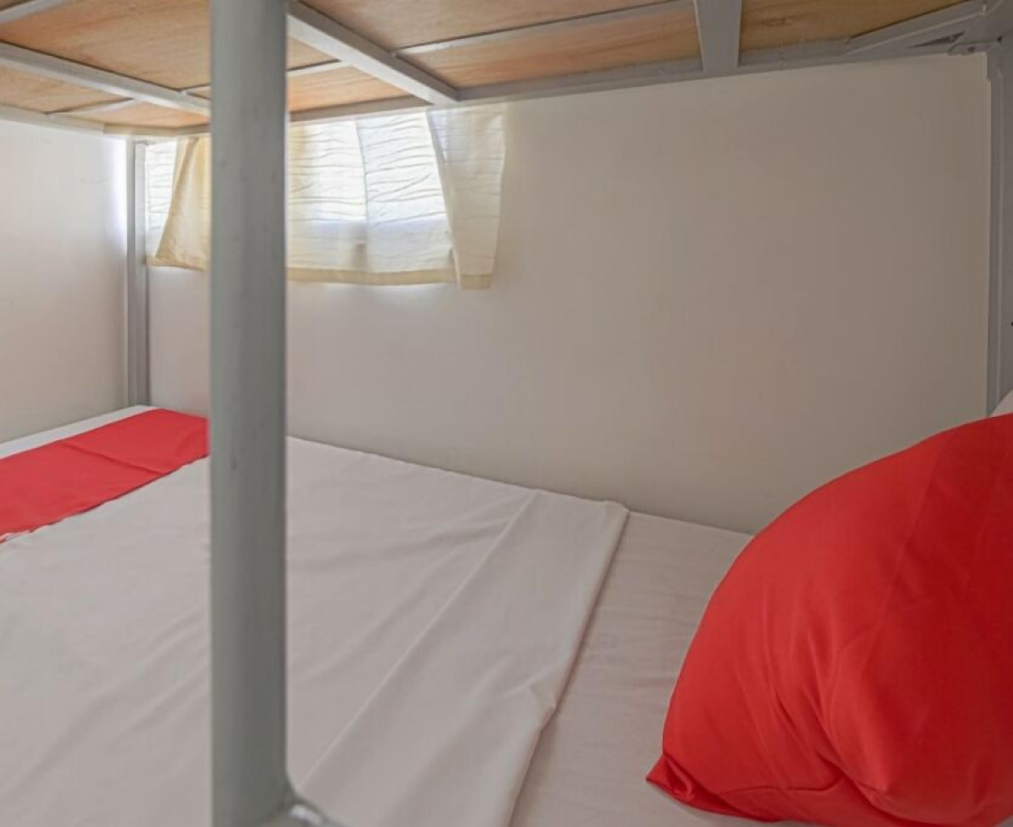 Una cama litera con un almohá de color rojo y una ventana con cortinas.