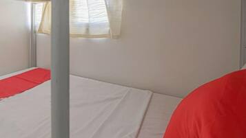 Una cama litera con un almohá de color rojo y una ventana con cortinas.
