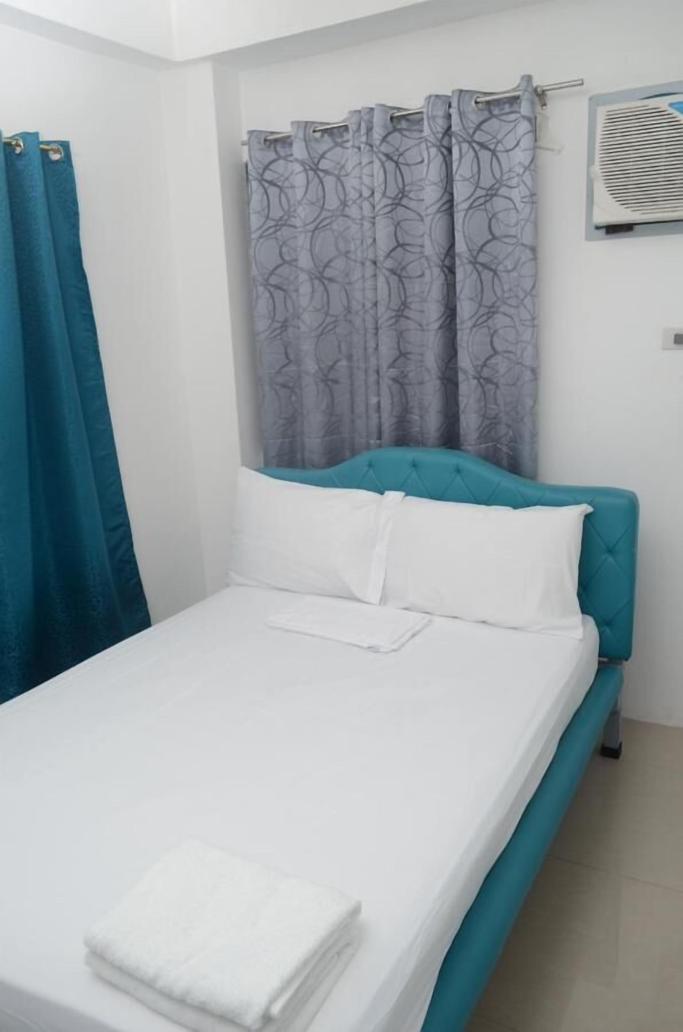 A single bed with a teal headboard, white bedding, and a folded white towel on the footboard.
