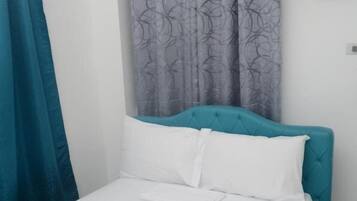 A single bed with a teal headboard, white bedding, and a folded white towel on the footboard.