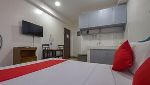 Una habitación de hotel con cama, escritorio, silla, televisor y kitchenette.