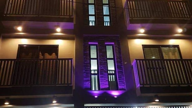 Un edificio de varios pisos con balcones, ventanas iluminadas y una entrada central con luz púrpura.