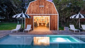 A wooden barn with a pool and lounge chairs in front.