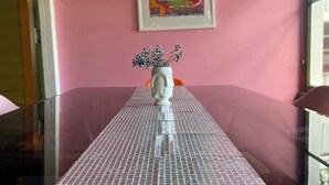 Une table à manger agrémentée d’un vase décoratif placé au centre, le tout adossé à un mur rose sur lequel est accrochée une œuvre d’art encadrée.