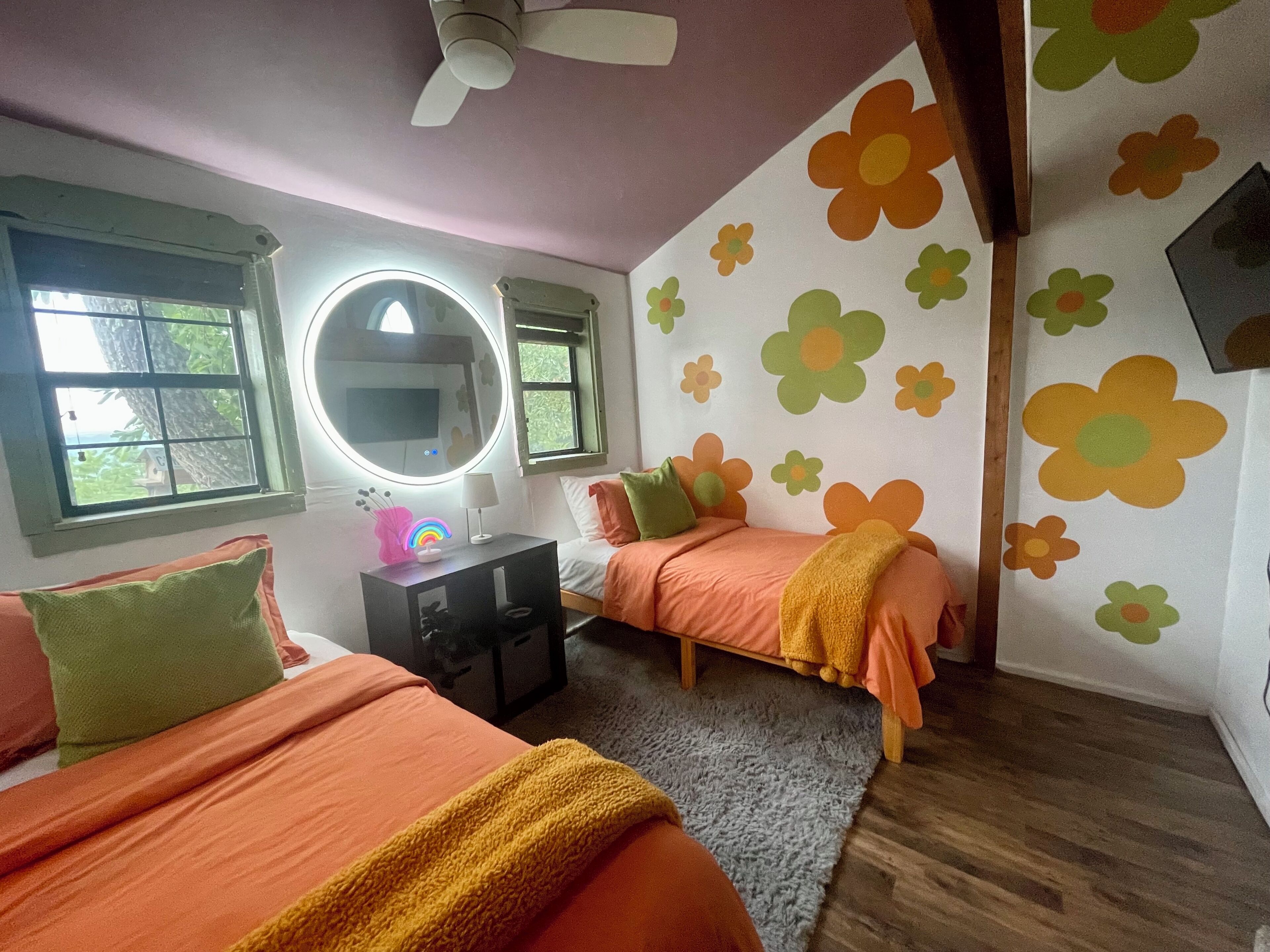 Ein Schlafzimmer mit zwei Betten, einem Deckenventilator, einem runden Spiegel und Wandmustern mit Blumen.