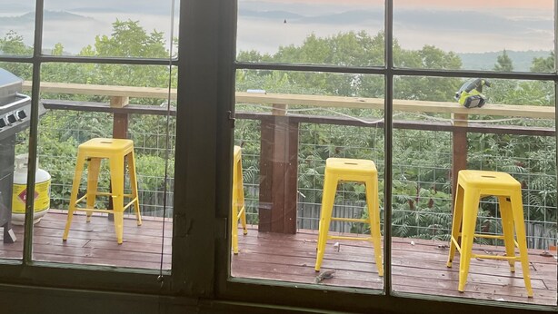 Un balcon avec des tabourets jaunes, un barbecue et une vue sur un paysage montagneux.