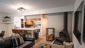 A modern living room with a sofa, coffee table, and fireplace. There is a kitchen area with wooden cabinets and a microwave. - The Ope! North Hideaway (Bellaire)