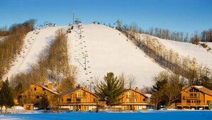 A snow-covered mountain with a ski lift and wooden cabins in the foreground. - The Ope! North Hideaway (Bellaire)