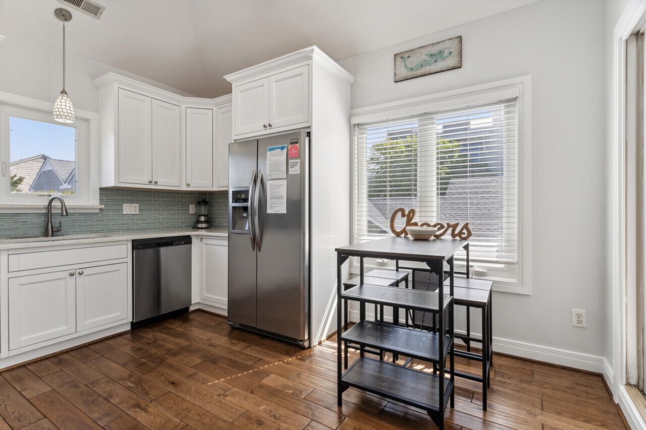 A kitchen with white cabinets, a stainless steel refrigerator, a dishwasher, and a window with blinds.