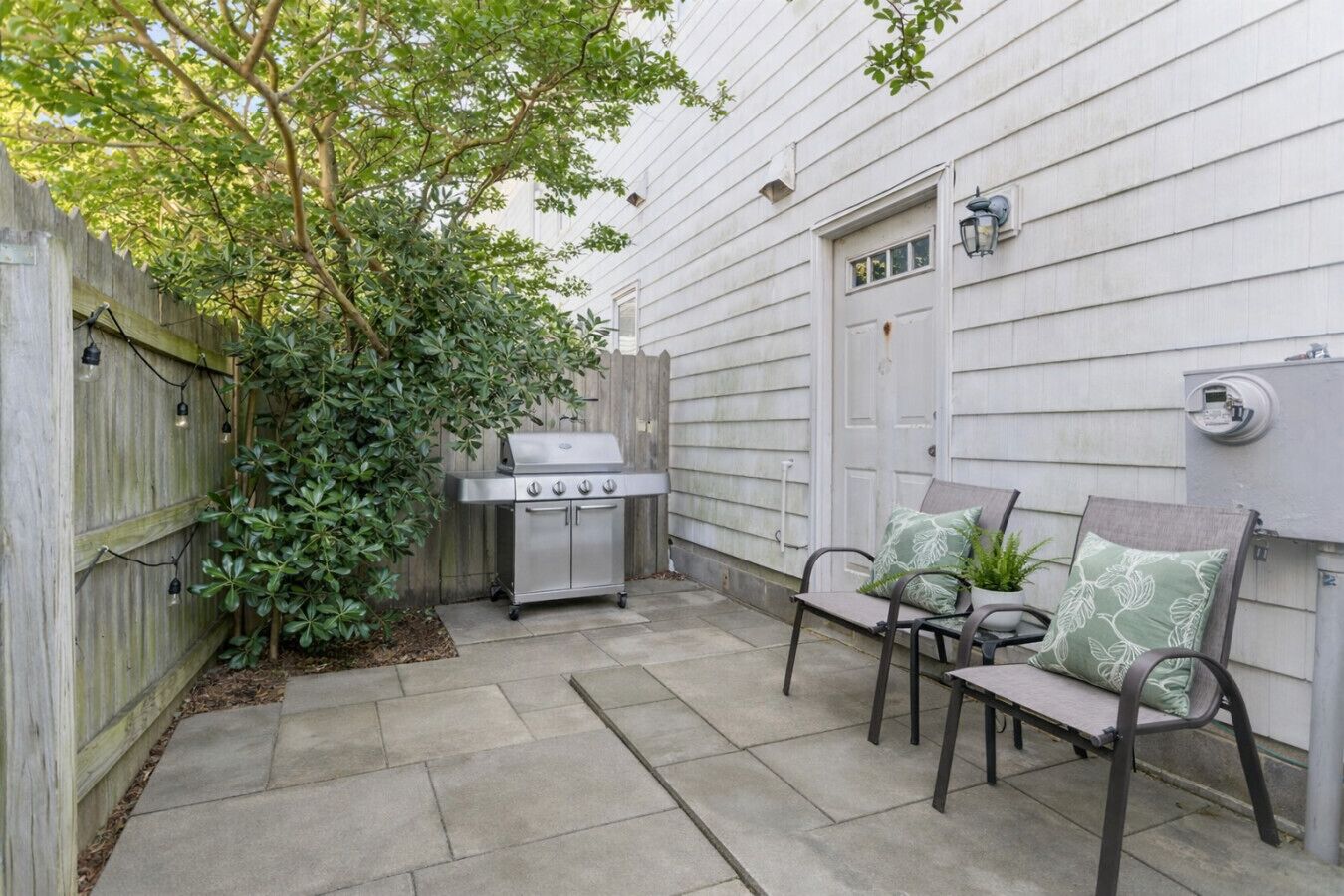 A patio with a grill, two chairs, and a wooden fence.