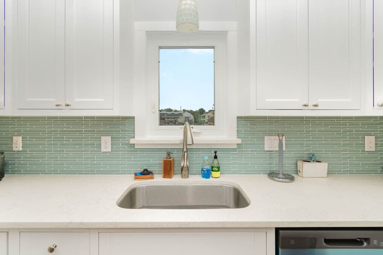 A kitchen with white cabinets, a window above the sink, and a green-tiled backsplash.