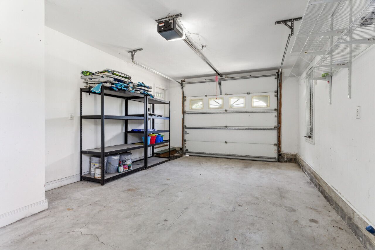A garage with a metal shelving unit containing paint cans and tools, a closed garage door, and a ceiling-mounted projector.