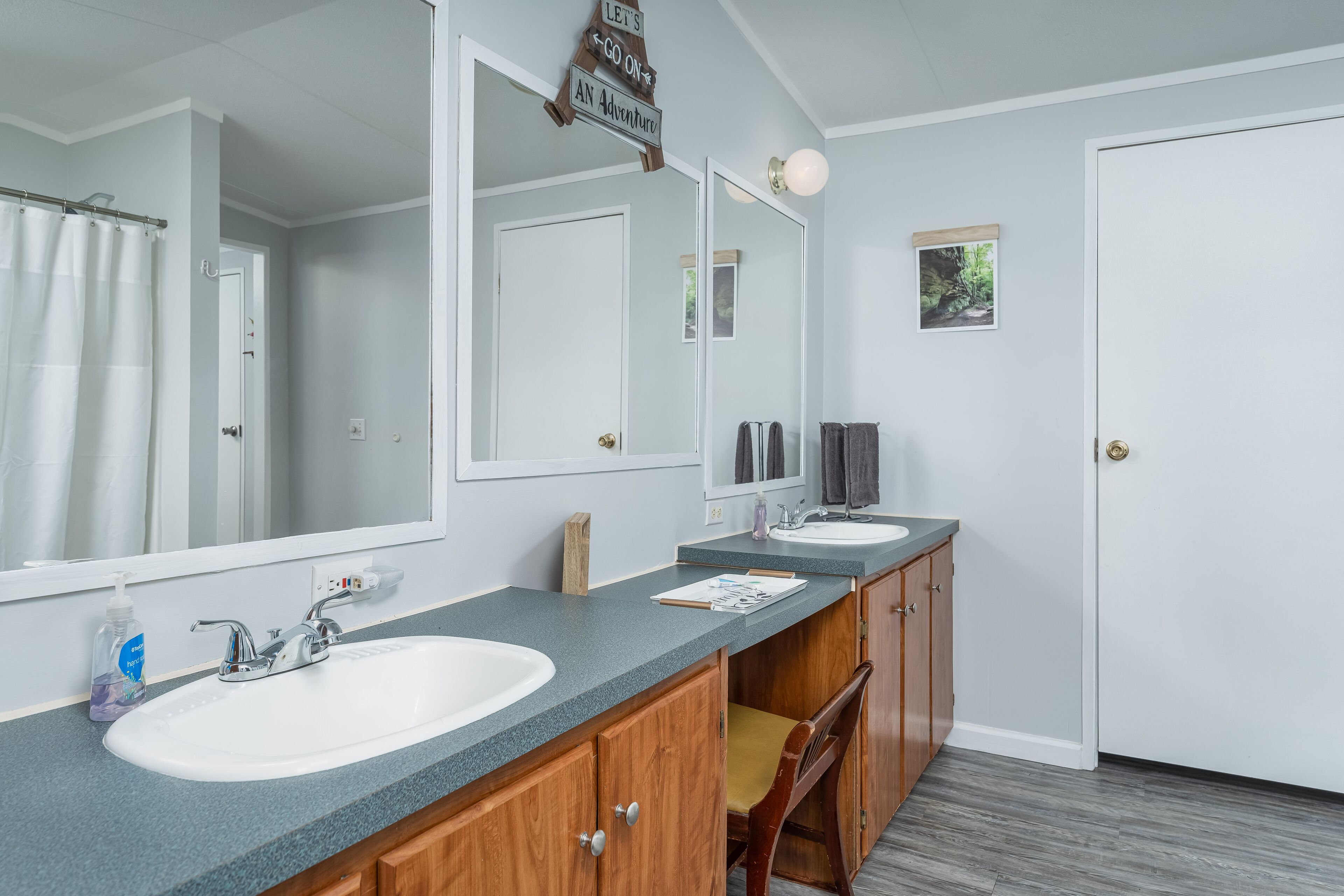 Une salle de bain avec deux lavabos, un grand miroir, un meuble en bois et une chaise.