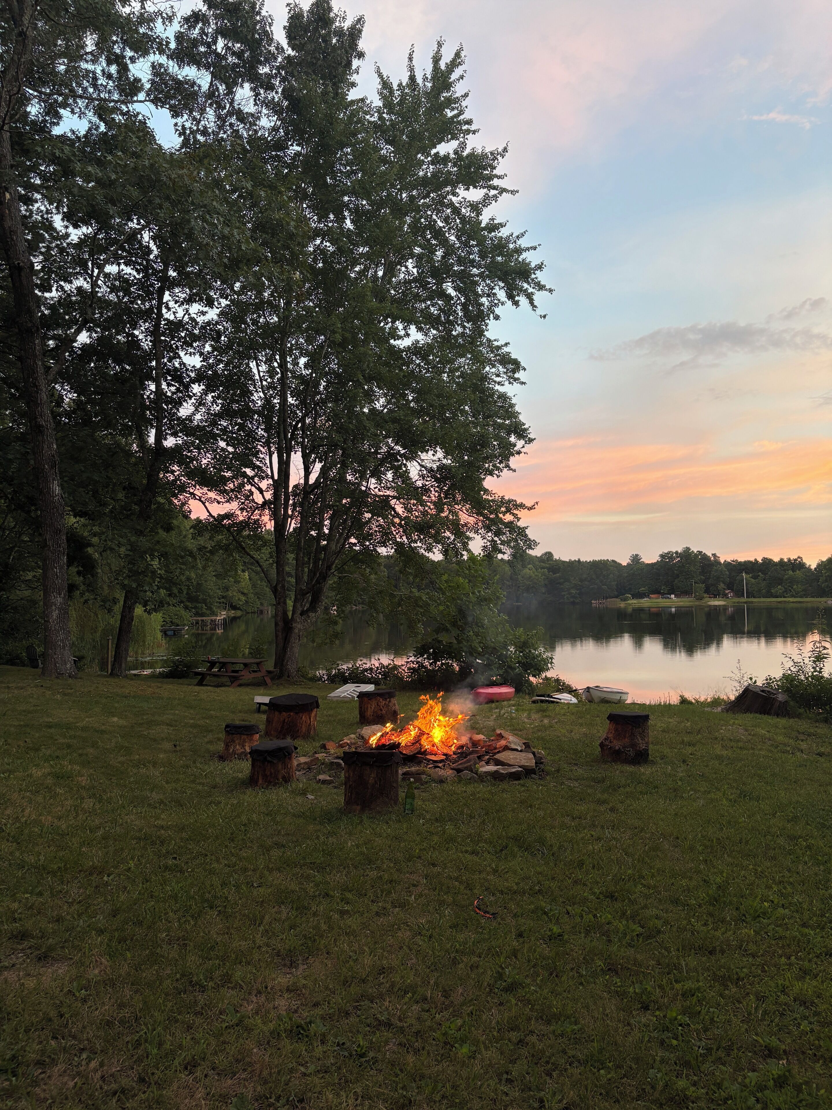 A lakeside campsite with a fire pit surrounded by trees and a picnic table.