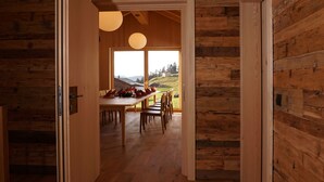 Un intérieur en bois comprenant un coin repas, des murs en bois et une vue sur l’extérieur par une porte ouverte.