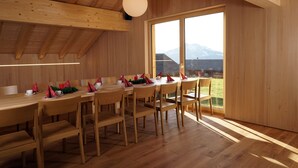 Un espace repas avec des tables et des chaises en bois, de grandes fenêtres offrant une vue sur les montagnes et un plafond en bois.