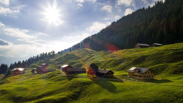Un paysage rural avec plusieurs maisons en bois situées sur des collines douces, entourées de forêts denses.