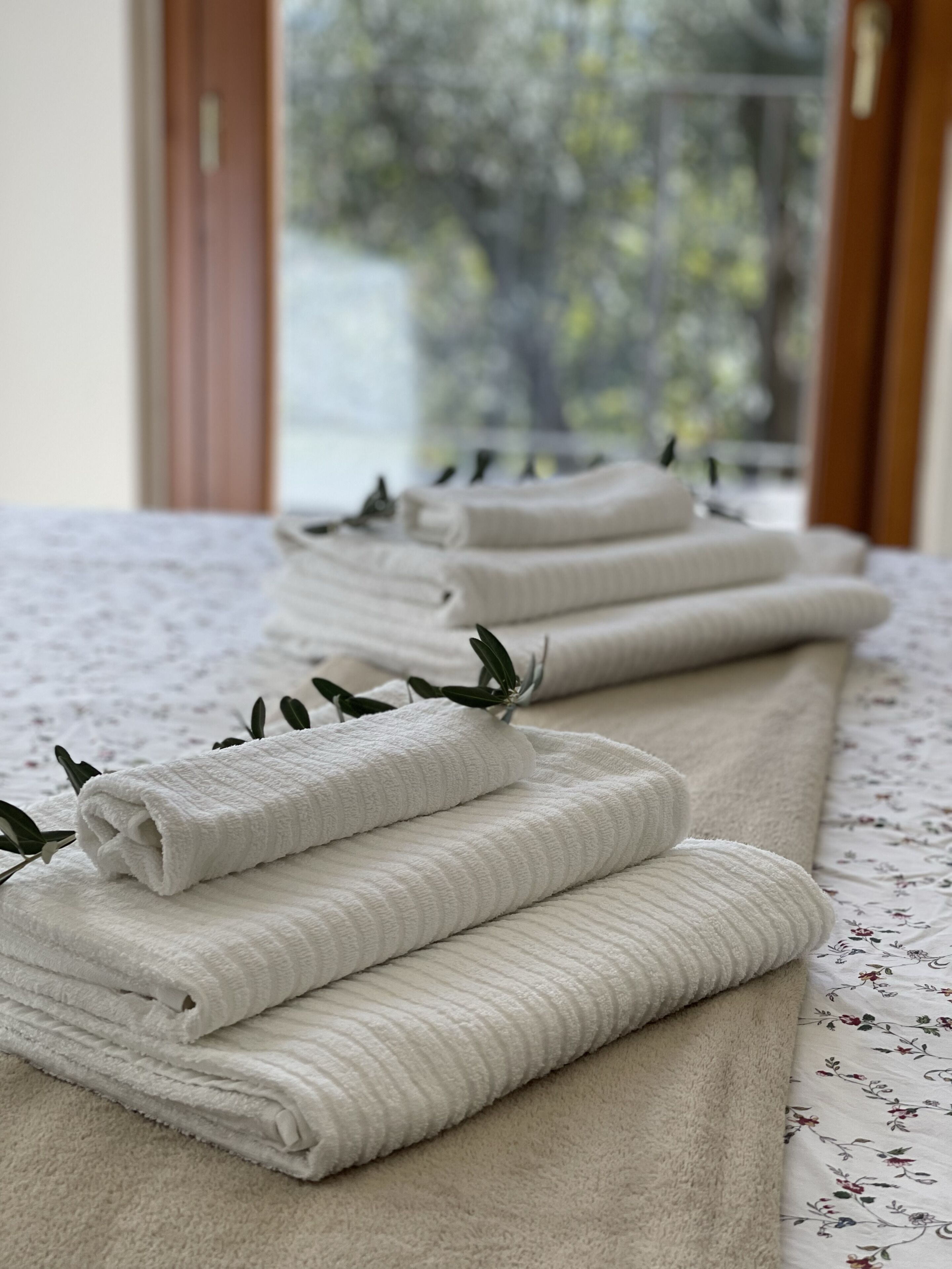 A neatly arranged row of folded towels on a bed with a floral-patterned bedspread.